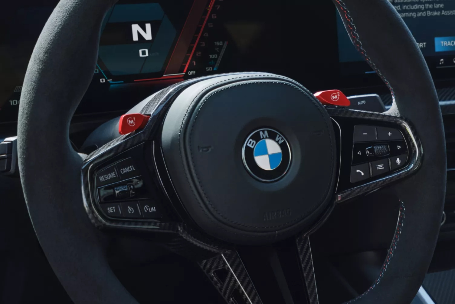 Close-up of BMW M Series steering wheel with red M1 and M2 buttons and digital instrument cluster.