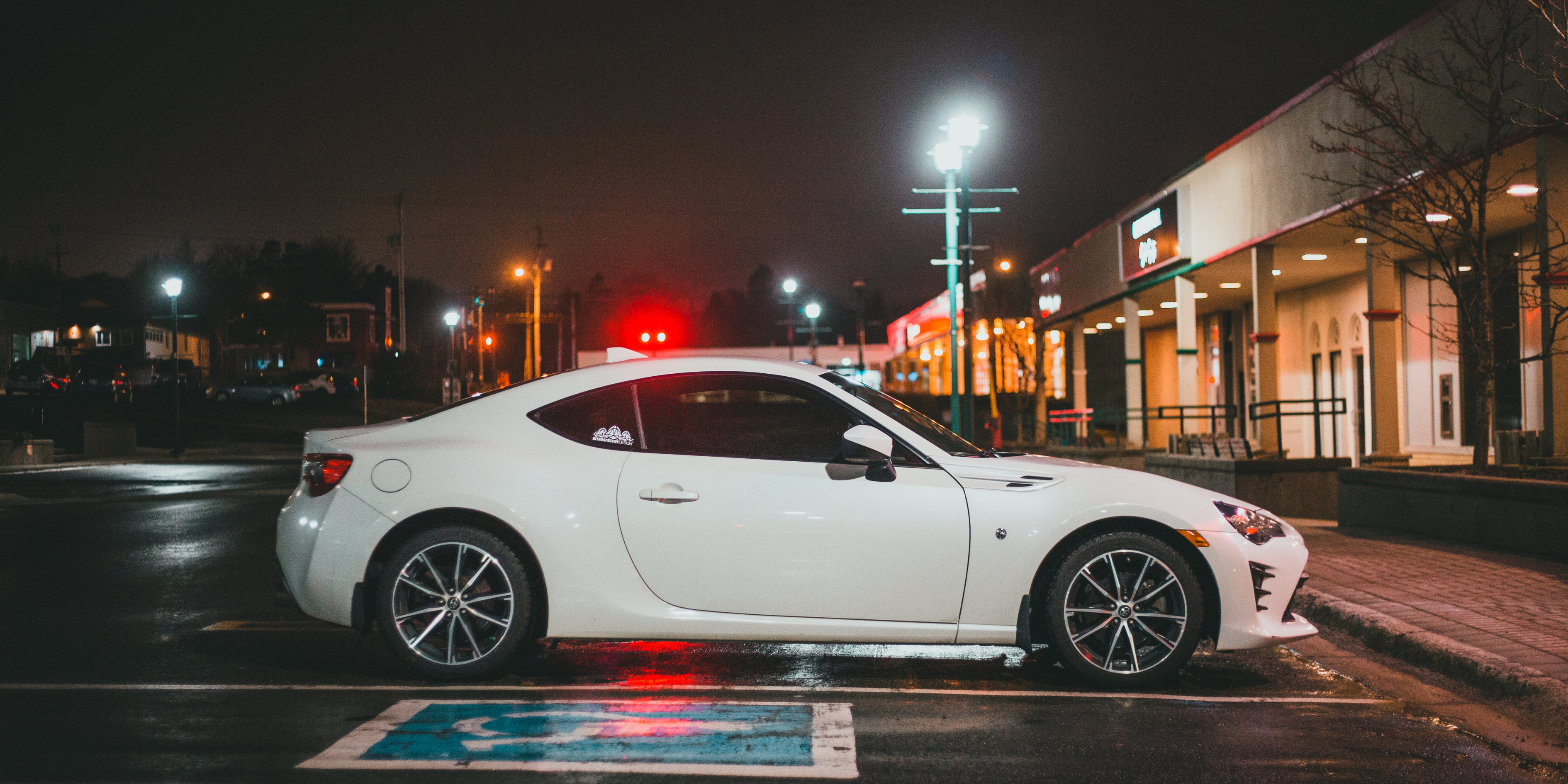White sports car parked in a shopping plaza at night.