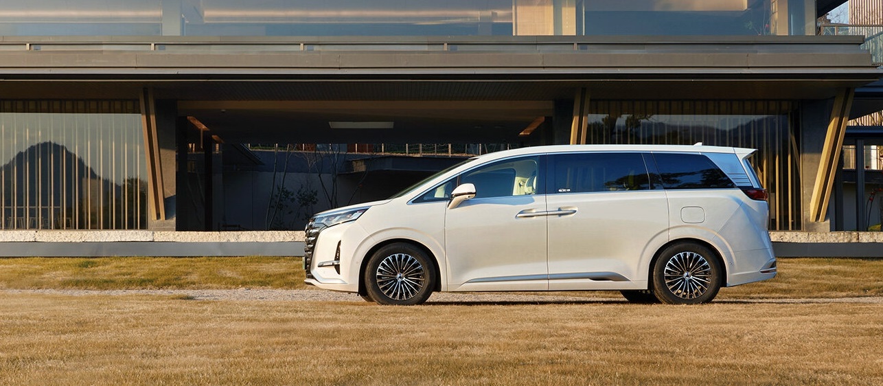 Side view of a white luxury MPV parked in front of a modern glass building.
