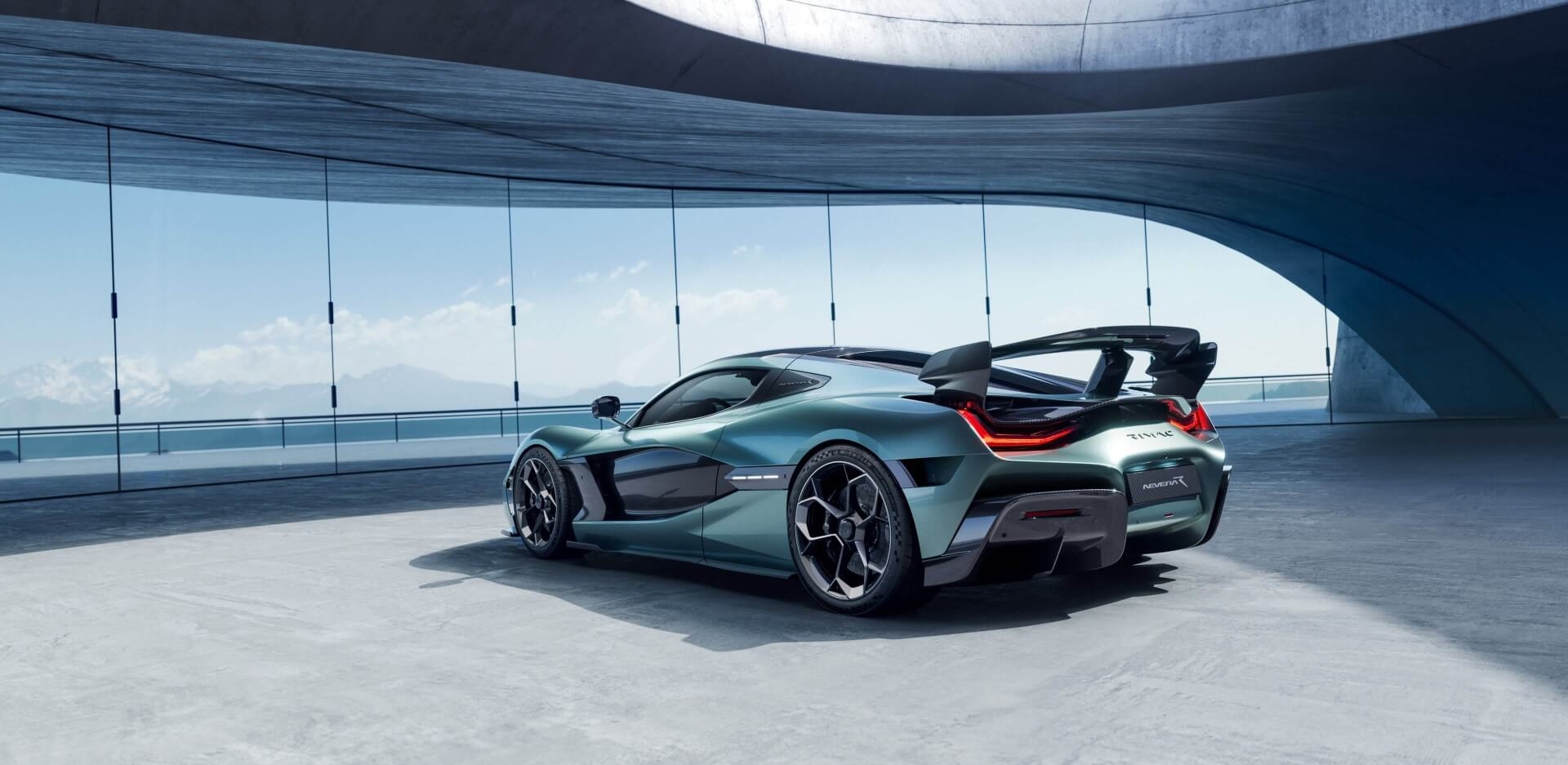 Rimac Nevera electric hypercar in teal shown from the rear three-quarter view inside a modern glass pavilion.